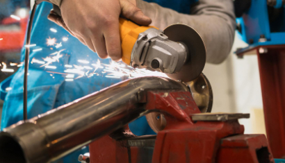 Pracownik produkcji tnie rurę metalową szlifierką kątową, widoczne iskry podczas cięcia